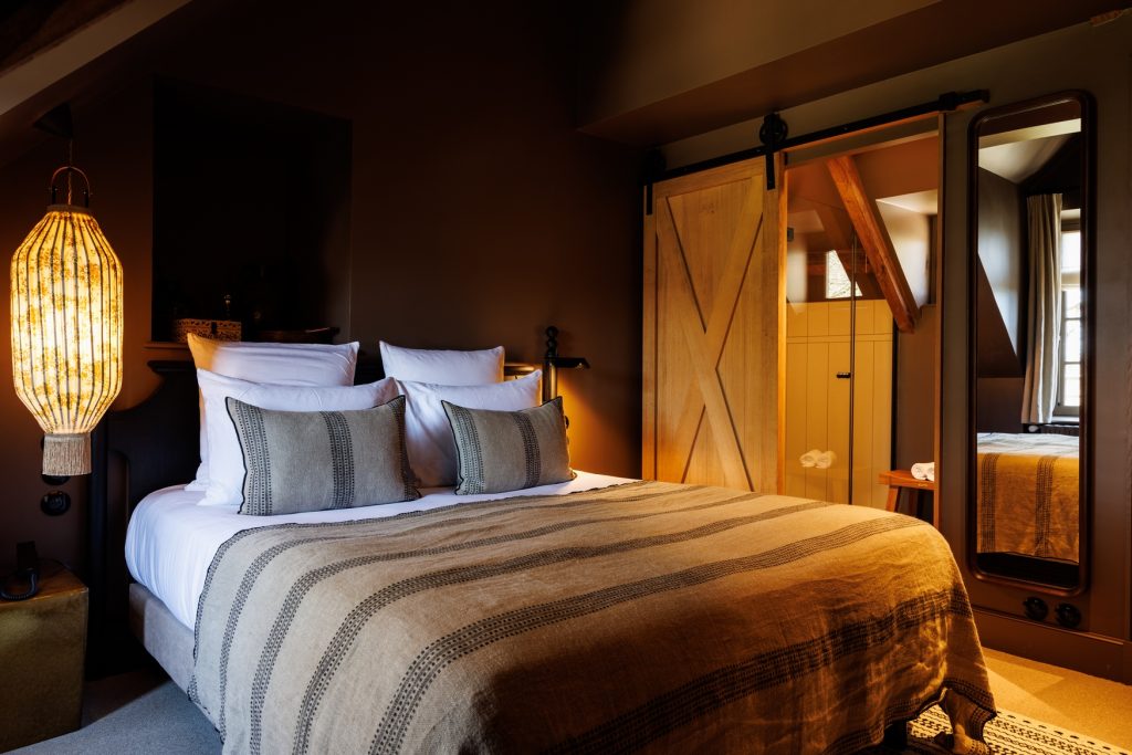 Lustre en tissu à frange éclairé suspendu au dessus du lit king size de la chambre coquette et sa salle de bain dans notre hotel deluxe en bretagne